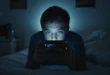 Joven adolescente mirando el celular en la oscuridad de su habitación