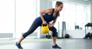 Mujer en ropa deportiva realizando entrenamiento de fuerza con una pesa rusa en un gimnasio iluminado