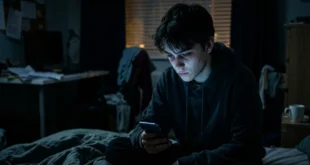 Persona joven mirando su smartphone en un entorno oscuro, reflejando el impacto en la salud mental.