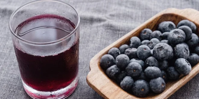 Vaso de jugo de arándano puro y bayas frescas sobre una mesa para evaluar su efecto en los dientes